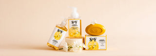 A collection of SOF Lemon Verbena soap products, including liquid soap pumps and a bar soap with packaging, arranged with white flowers on a neutral background.