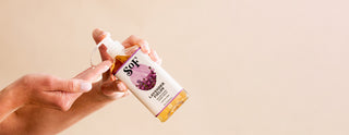 A person dispenses SOFT brand lavender hand soap from a pump bottle onto their finger, against a plain light background.
