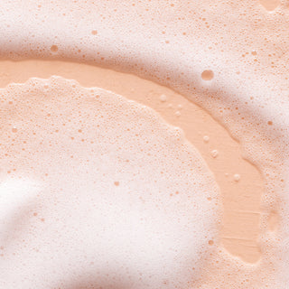 Close-up of Orange Blossom & Honey Hydrating Foaming Hand Wash shows light orange, creamy foam with frothy bubbles in circular patterns, giving a smooth, airy texture and soft abstract visual effect.