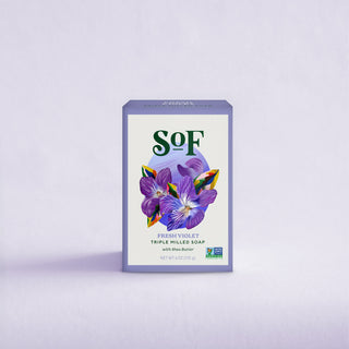 A purple box of Fresh Violet Moisturizing Bar Soap features violet floral art and green text, set on a light purple background. Enjoy its creamy lather and organic shea butter for gentle, nourishing skincare.