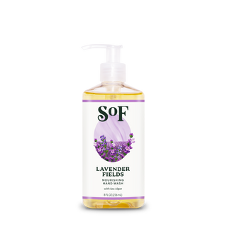 A clear plastic pump bottle of Lavender Fields Nourishing Hand Wash with sea algae, featuring a paraben-free label decorated with purple lavender flowers on a soft purple background; contains yellow liquid.