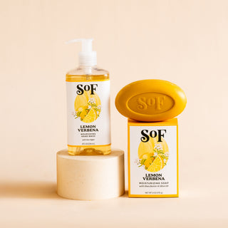 Lemon Verbena Liquid Hand Soap and Bar Soap are showcased on a light round pedestal against a beige background. Their packaging features lemons and greenery, making these SoF essentials perfect for your daily cleanse.