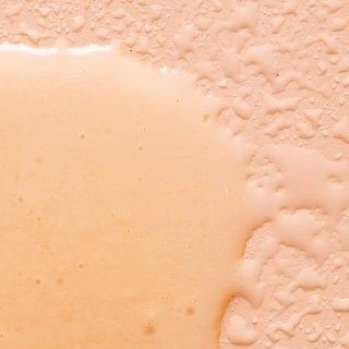 Close-up of Lemon Verbena Nourishing Hand Wash, a beige, creamy cleanser spread on a textured surface, showing smooth and bubbled areas—evoking a rich lather infused with essential oils.