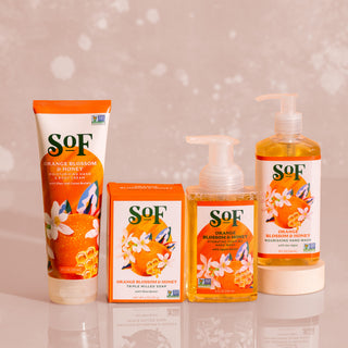 The Orange Blossom & Honey Bundle features four bath products—a tube, a box, a foaming hand soap, and a pump hand soap—arranged in a row against a softly blurred light background.