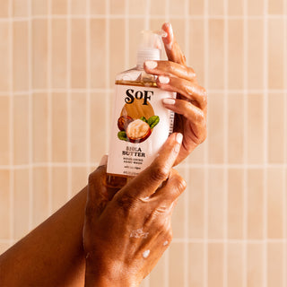 A person with vitiligo presses the pump on a bottle of Shea Butter Nourishing Hand Wash against a tiled bathroom wall.